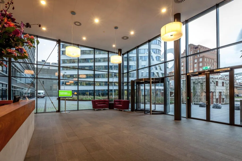 Moderne entreehal van een kantoorpand aan de Prinses Beatrixlaan met glazen gevel, zitgedeelte en automatische draaideur.